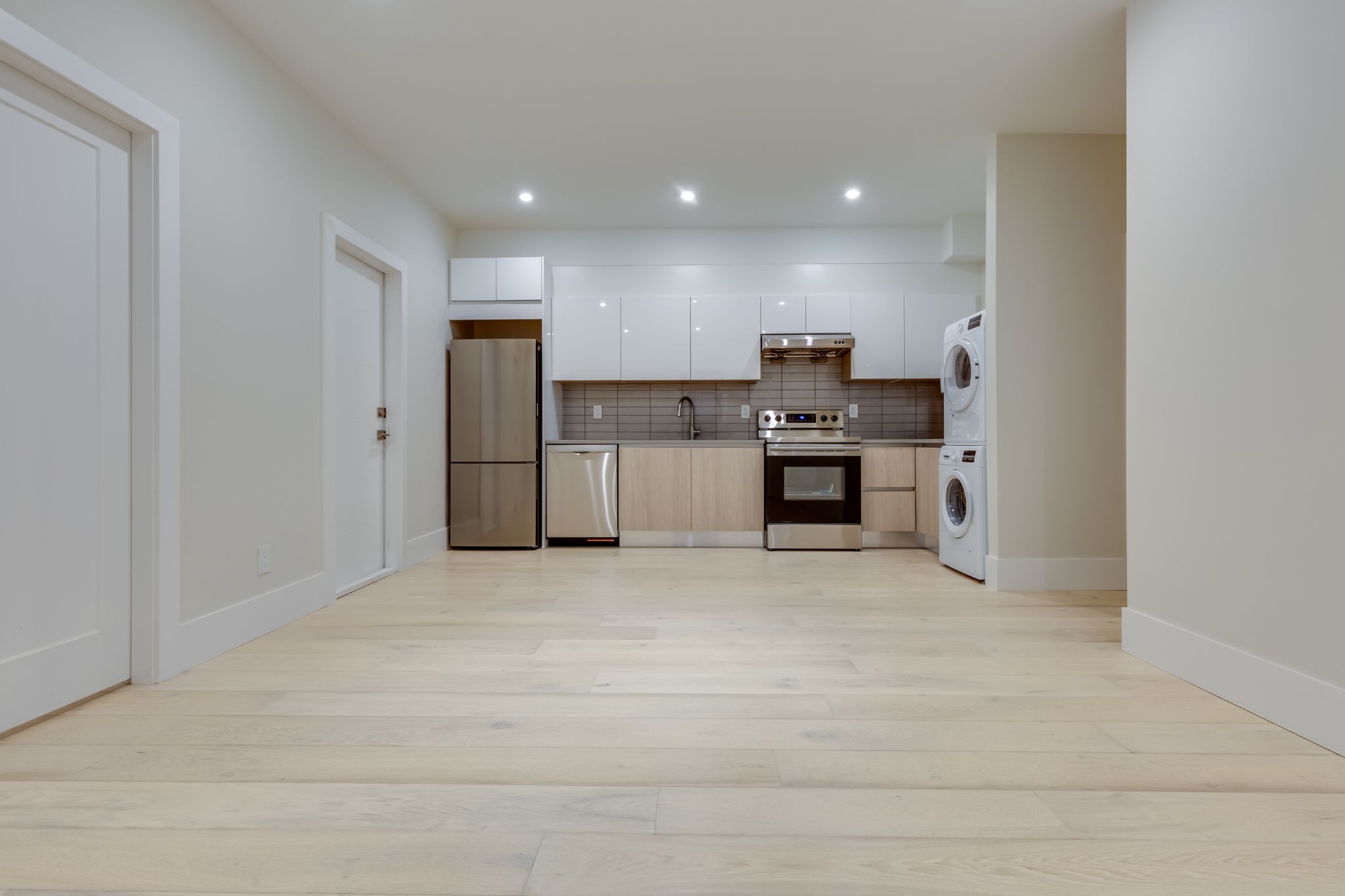 Modern basement apartment kitchen with stainless steel appliances and stacked laundry unit