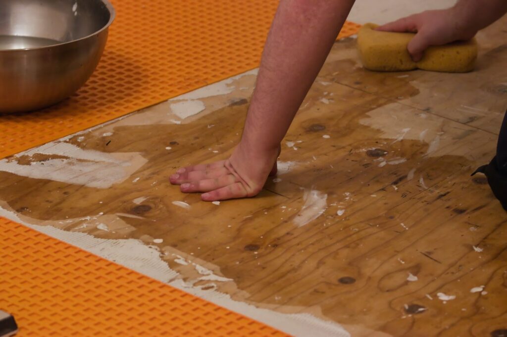 A person cleaning a wooden floor in a basement using a sponge