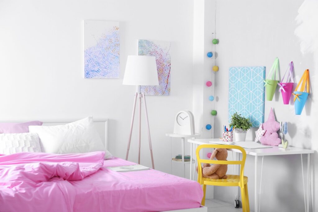 A vibrant pink bed with a white desk and colorful decorations in a basement bedroom setting.