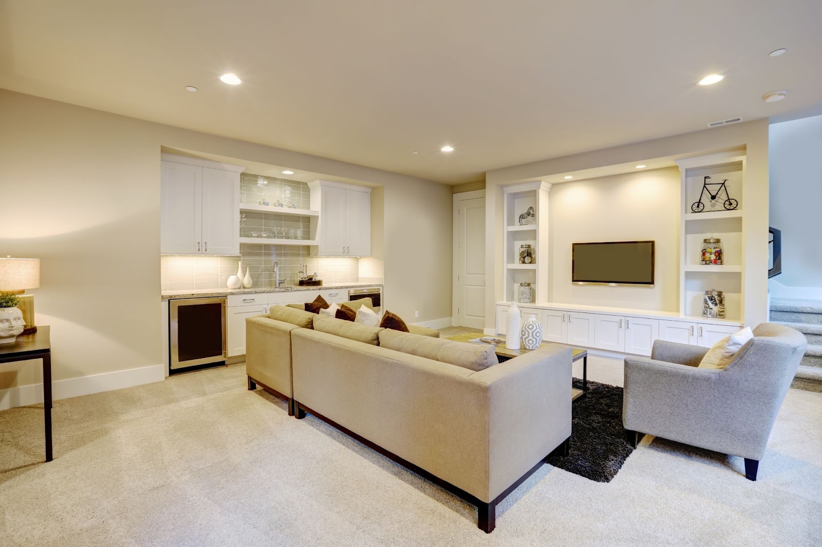 Modern living room with beige sectional sofa, TV, and built-in shelves.