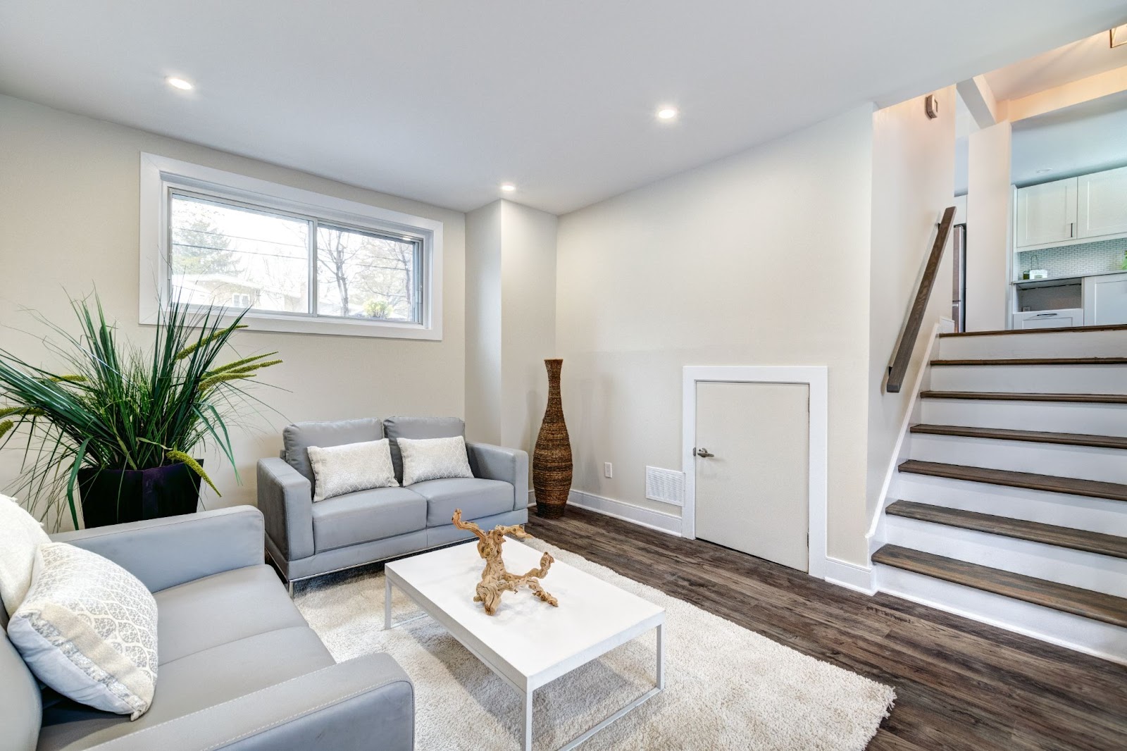 Modern living room with gray sofas, white coffee table, and staircase.