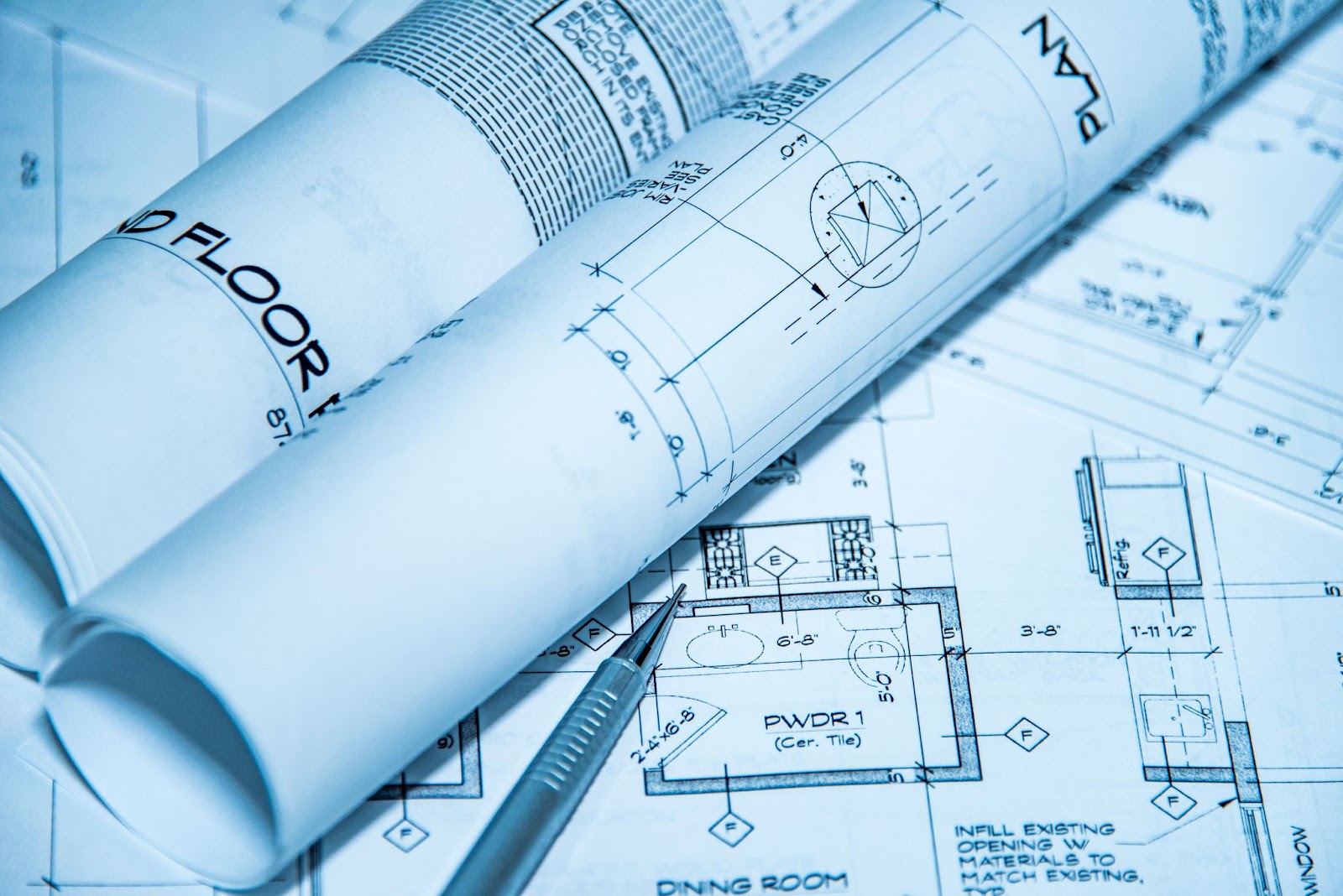 Rolled architectural blueprints with a pencil, showing a second floor plan including a dining room