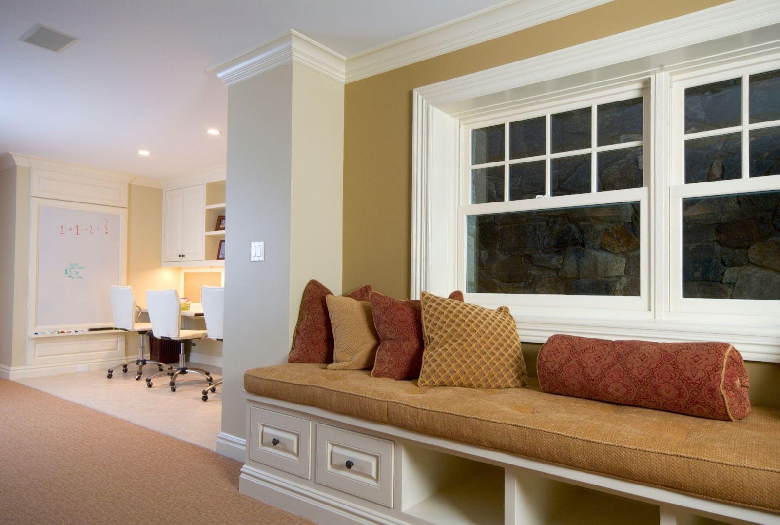 A cozy home office featuring a window seat beside a neatly organized desk illuminated by natural light
