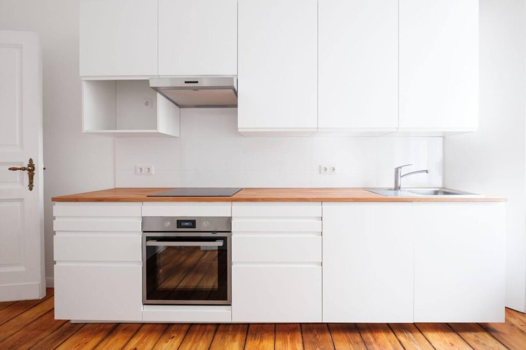 A bright kitchen featuring white cabinets and wooden floors exuding a clean and modern aesthetic