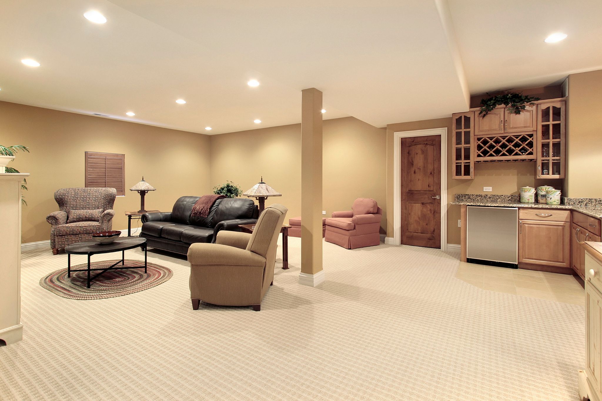 A spacious finished basement featuring a carpeted living area with a leather sofa, armchairs, and a wet bar with oak cabinetry.