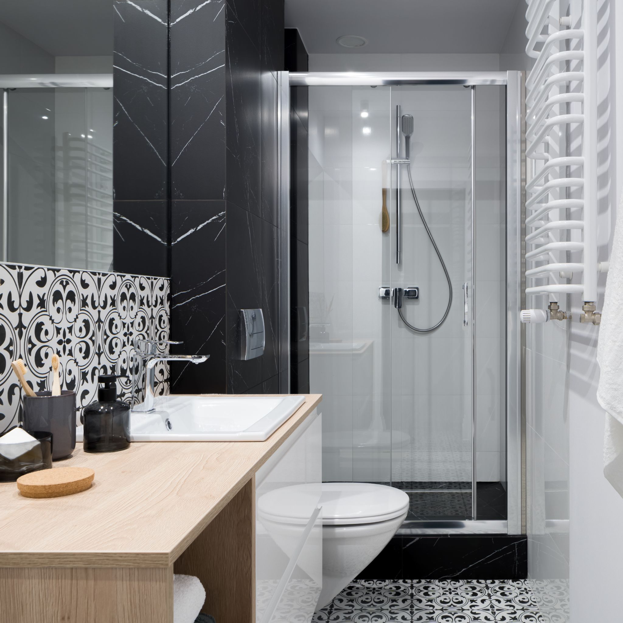 A modern bathroom with a wooden vanity, a toilet, a glass-enclosed shower, and black and white patterned tile flooring.