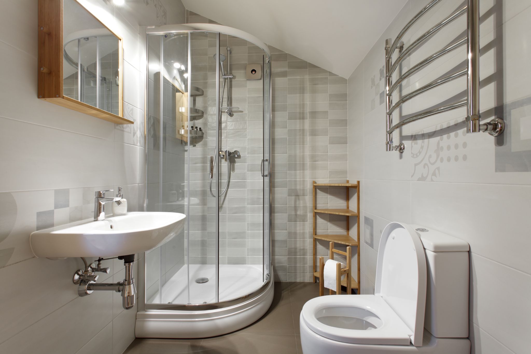 A modern, compact bathroom featuring a curved glass corner shower, a wall-mounted sink, and a toilet.